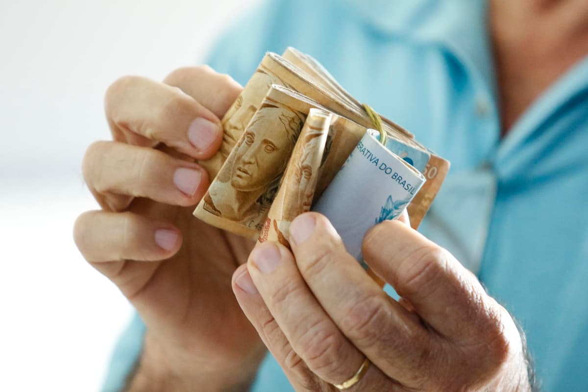 Mãos de idoso que prendem notas reais brasileiras-dinheiro de Brasil